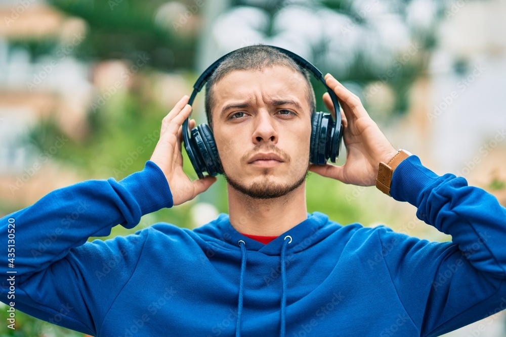 Young hispanic man with serious expression using headphones at the city Young hispanic man with serious expression using headphones at the city