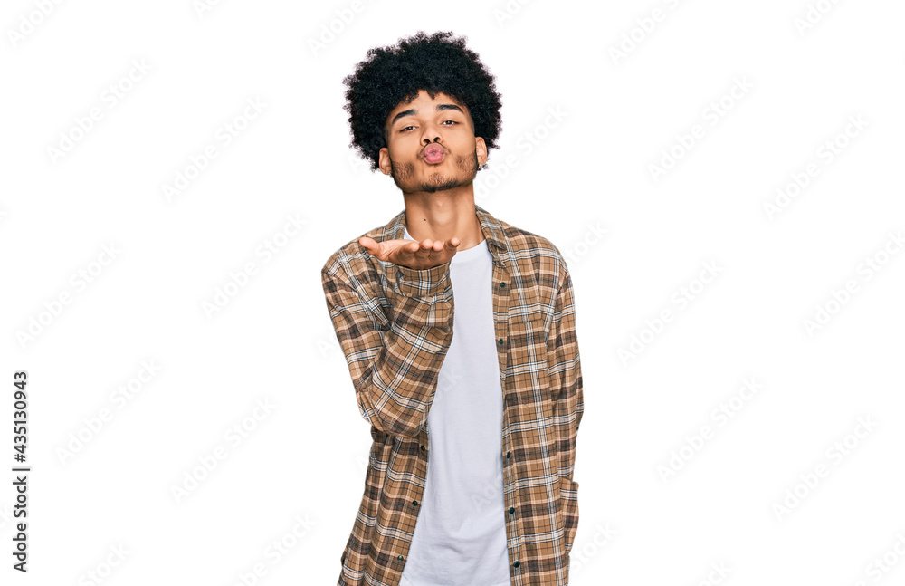 Young african american man with afro hair wearing casual clothes looking at the camera blowing a kiss with hand on air being lovely and sexy. love expression. Young african american man with afro hair wearing casual clothes looking at the camera blowing a kiss with hand on air being lovely and sexy. love expression.
