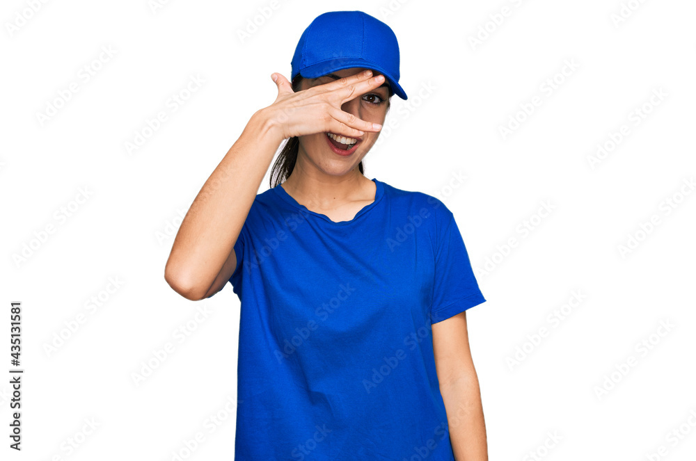 Young hispanic girl wearing delivery courier uniform peeking in shock covering face and eyes with hand, looking through fingers with embarrassed expression. Young hispanic girl wearing delivery courier uniform peeking in shock covering face and eyes with hand, looking through fingers with embarrassed expression.