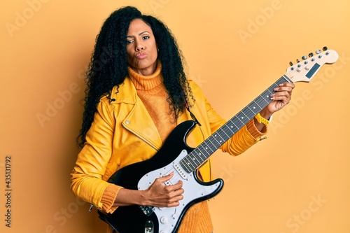 Middle age african american woman playing electric guitar looking at the camera blowing a kiss being lovely and sexy. love expression.