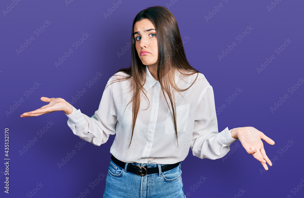 Young brunette teenager wearing business white shirt clueless and confused expression with arms and hands raised. doubt concept. Young brunette teenager wearing business white shirt clueless and confused expression with arms and hands raised. doubt concept.