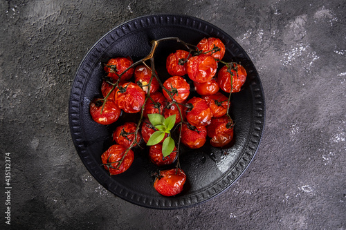 Black plate with confit tomatoes on dark background photo