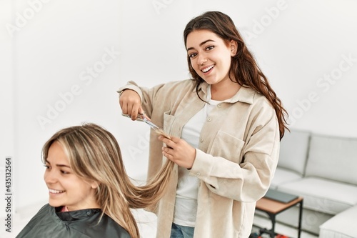 Young woman cutting hair to her girlfriend at home.