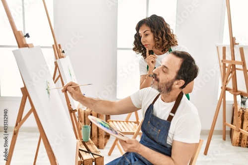 Middle age student and teacher with serious expression painting at art school.