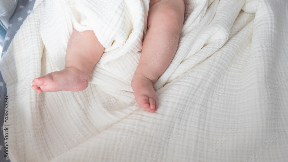 New born tiny feet in a pastel white blanket. Unrecognisable girl kid laying in the bed. Close up, copy space. New born tiny feet in a pastel white blanket. Unrecognisable girl kid laying in the bed. Close up, copy space.