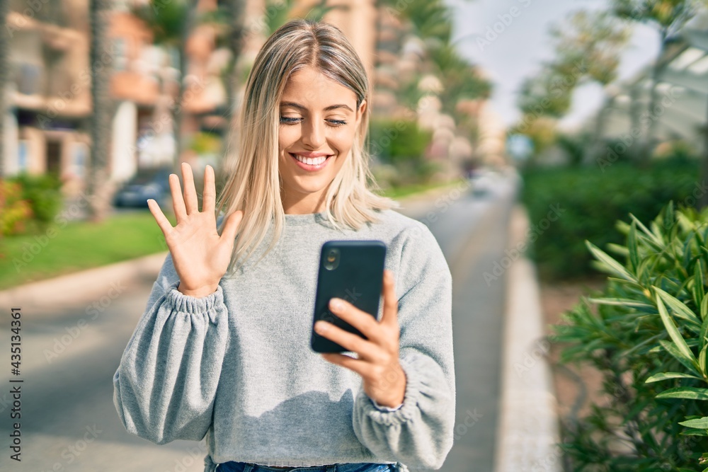 Young blonde girl smiling happy doing video call using smartphone at the city
