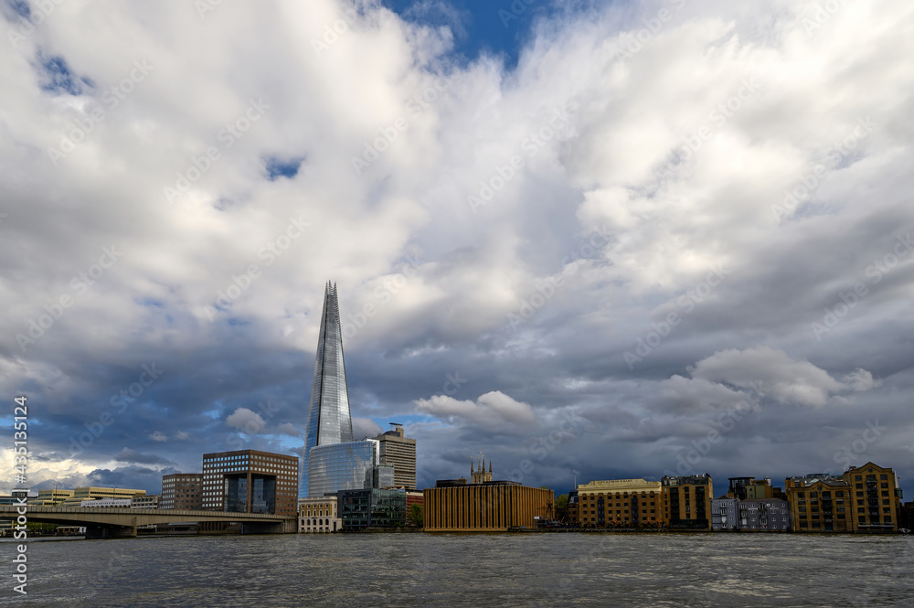 Obraz premium London, UK: View from the City of London looking south across the River Thames with London Bridge and the Shard building. Light reflecting on The Shard with dark storm clouds behind.