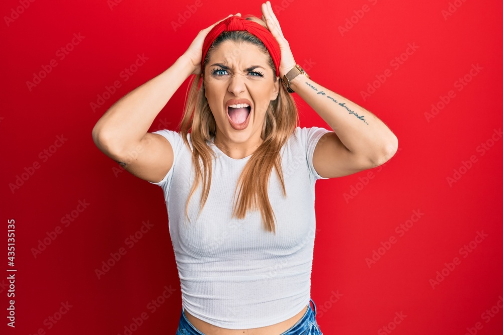 Young caucasian woman wearing casual white t shirt crazy and scared with hands on head, afraid and surprised of shock with open mouth Young caucasian woman wearing casual white t shirt crazy and scared with hands on head, afraid and surprised of shock with open mouth