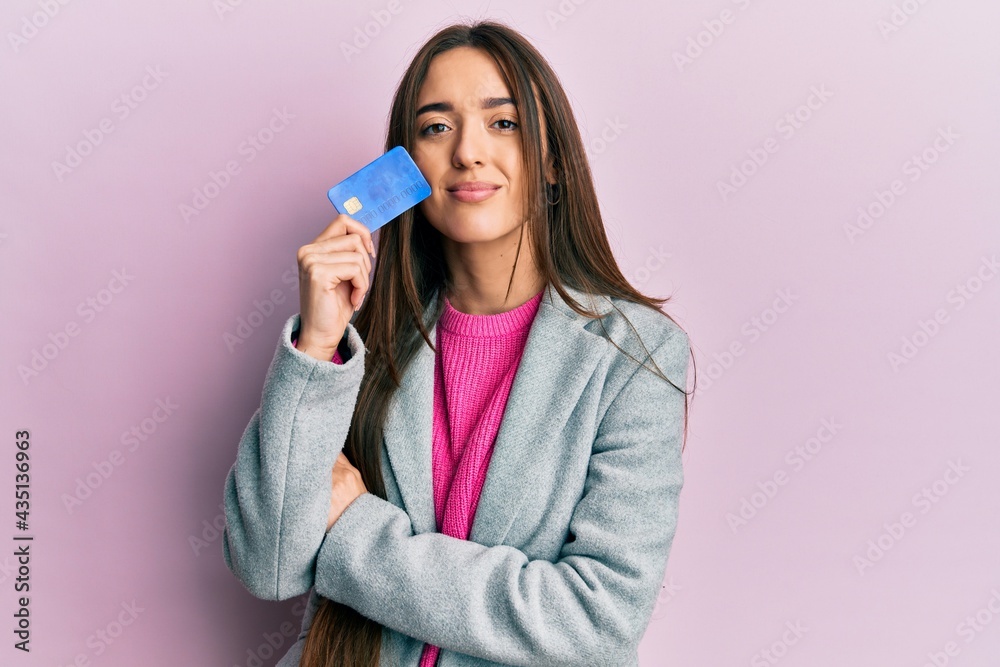 Young hispanic girl holding credit card relaxed with serious expression on face. simple and natural looking at the camera. Young hispanic girl holding credit card relaxed with serious expression on face. simple and natural looking at the camera.