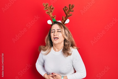 Middle age caucasian woman wearing cute christmas reindeer horns with hand on stomach because nausea, painful disease feeling unwell. ache concept.