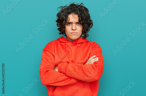 Young hispanic woman with curly hair wearing casual sweatshirt skeptic and nervous, disapproving expression on face with crossed arms. negative person.