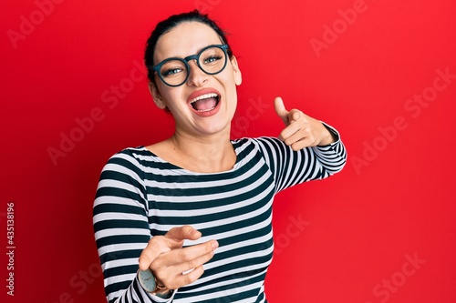 Young caucasian woman wearing casual clothes and glasses pointing fingers to camera with happy and funny face. good energy and vibes.