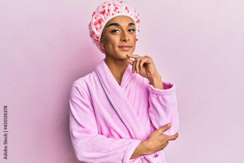 Hispanic man wearing make up wearing shower towel cap and bathrobe looking confident at the camera smiling with crossed arms and hand raised on chin. thinking positive. Hispanic man wearing make up wearing shower towel cap and bathrobe looking confident at the camera smiling with crossed arms and hand raised on chin. thinking positive.