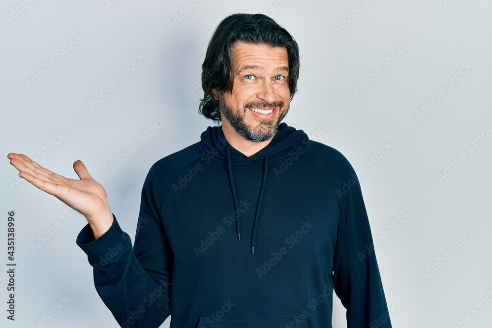 Middle age caucasian man wearing casual sweatshirt smiling cheerful presenting and pointing with palm of hand looking at the camera.