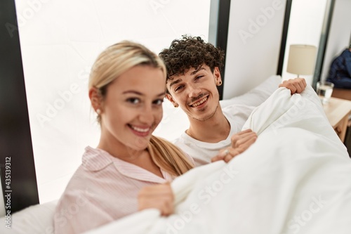 Young beautiful couple lying in bed and covering with blanket at home.