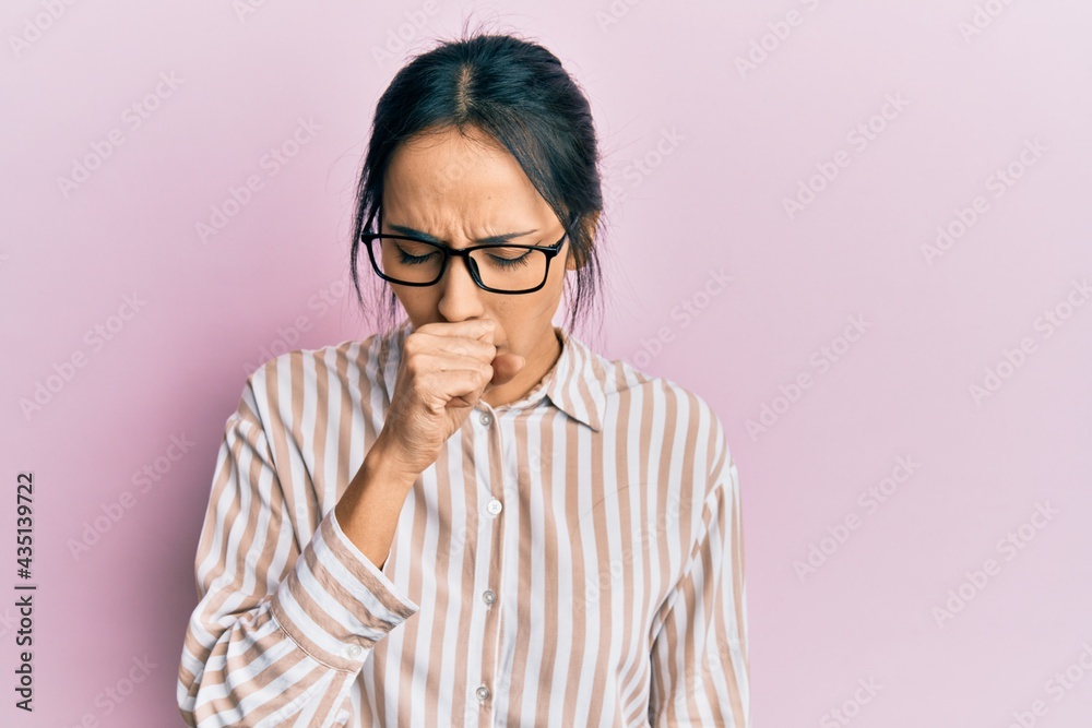Young hispanic girl wearing casual clothes and glasses feeling unwell and coughing as symptom for cold or bronchitis. health care concept. Young hispanic girl wearing casual clothes and glasses feeling unwell and coughing as symptom for cold or bronchitis. health care concept.