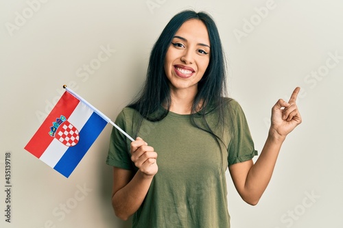 Young hispanic girl holding croatia flag smiling happy pointing with hand and finger to the side