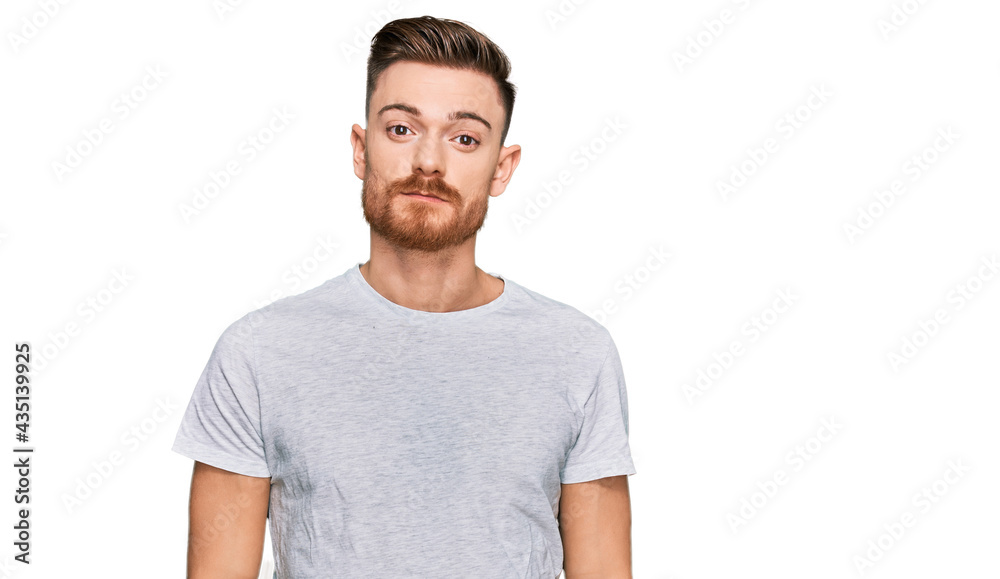 Young redhead man wearing casual grey t shirt relaxed with serious expression on face. simple and natural looking at the camera. Young redhead man wearing casual grey t shirt relaxed with serious expression on face. simple and natural looking at the camera.