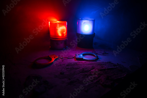 Police raid at night and you are under arrest concept. Silhouette of handcuffs with police car on backside. Image with the flashing red and blue police lights at foggy background.
