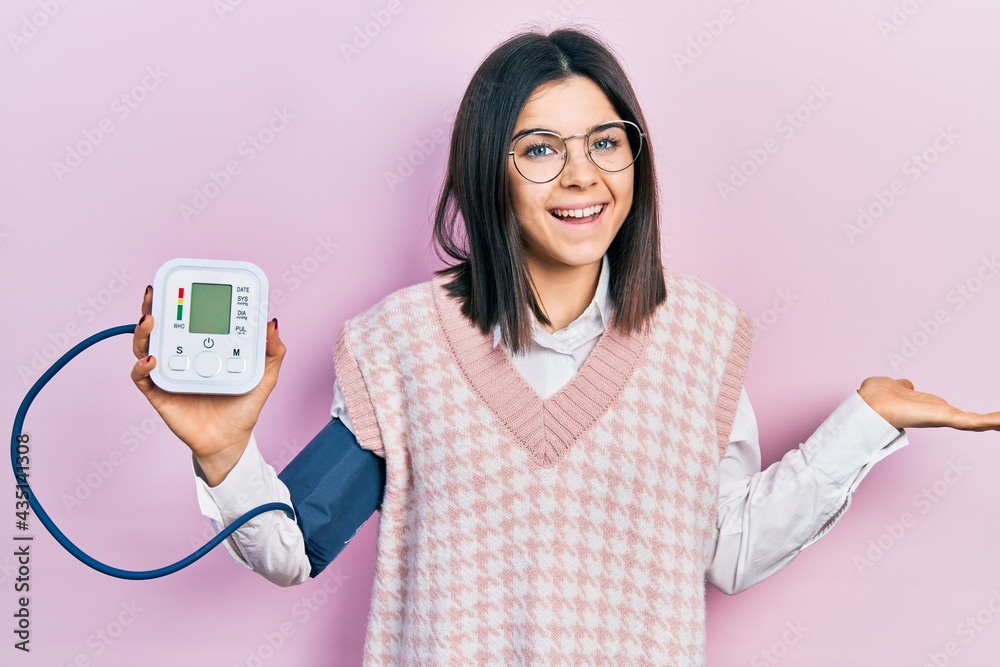 Young brunette woman using blood pressure monitor celebrating achievement with happy smile and winner expression with raised hand Young brunette woman using blood pressure monitor celebrating achievement with happy smile and winner expression with raised hand