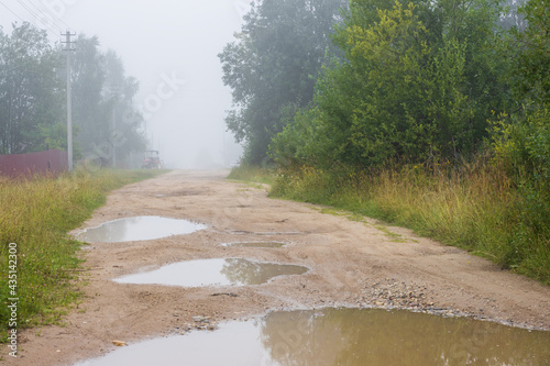 Country road view. Foggy rural landscape. Puddles on a dirt road. Morning fog. Poor visibility in fog.