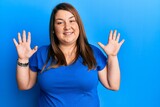 Beautiful brunette plus size woman wearing casual blue t shirt showing and pointing up with fingers number ten while smiling confident and happy.