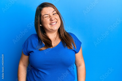Beautiful brunette plus size woman wearing casual blue t shirt winking looking at the camera with sexy expression, cheerful and happy face. © Krakenimages.com