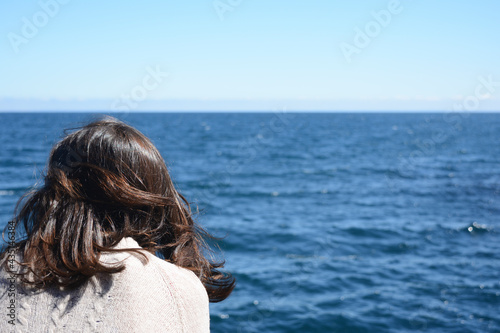 woman from behind looking at the water of a lake or deep blue sea