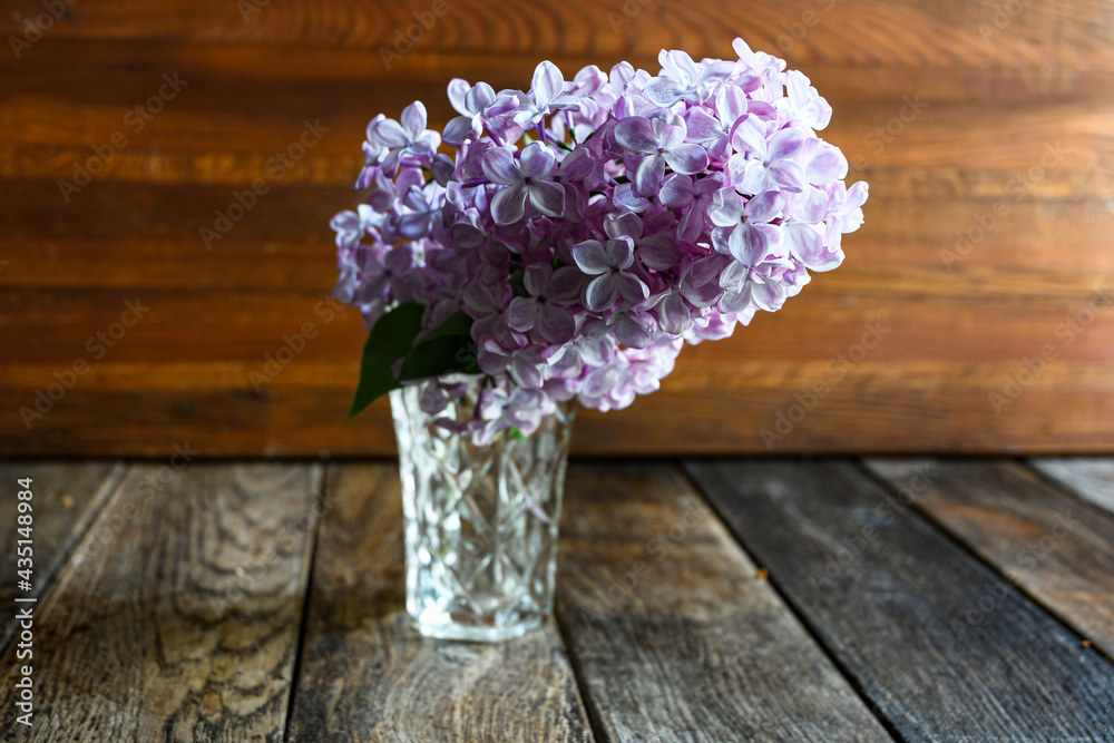 Lilac branches in a crystal vase on a wooden background. Lilac branches in a crystal vase on a wooden background.