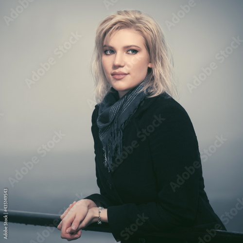 Young fashion woman in black coat leaning on railing in a fog