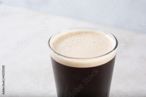 A view of a glass of either cold brew coffee with a nitro head or a dark stout style beer with a full frothy head.