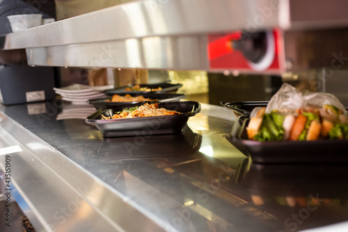 A view of prepared to-go food order containers resting inside a pass-through window in a restaurant kitchen setting.