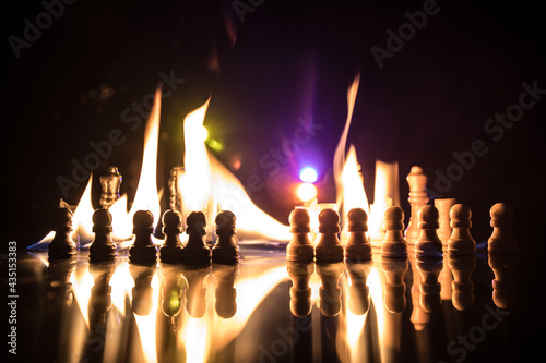 Сhess pieces on the chessboard against the background of a burning fire.