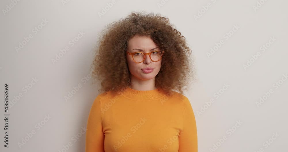 Strict curly haired young European woman shakes finger says no forbids you to do something wears optical spectacles and orange jumper shakes head isolated over white background. I prohibit this