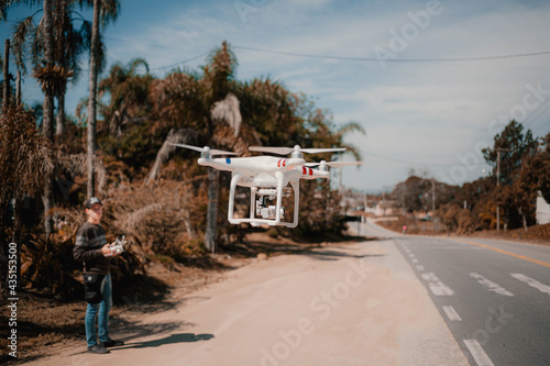 Flying drone with blurred pilot in the background. Houvering aircraft on street. Aerial video © Ricardo