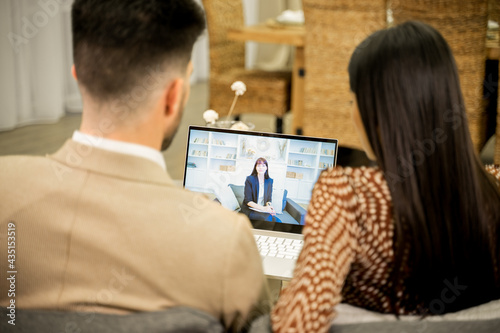 Rear view of young family couple having online consultation with psychologist, wife and husband looking at laptop screen and complaining about problems and misunderstanding in relationships