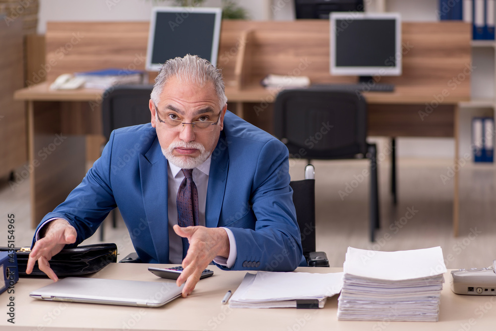 Old businessman employee in wheel-chair working in the office Old businessman employee in wheel-chair working in the office
