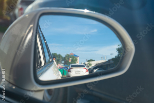 Blurred mirror wing of white car with reflection of cars and people in the community market during the day. © thongchainak