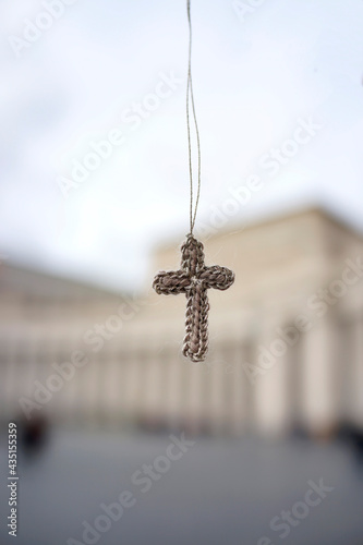 A knitted cross hangs in the sky before historic buildings in Vatican City.