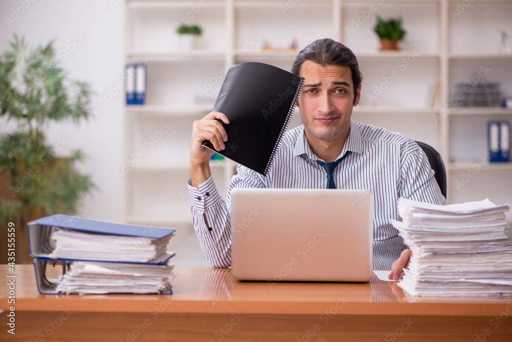 Young male employee unhappy with excessive work in the office Young male employee unhappy with excessive work in the office
