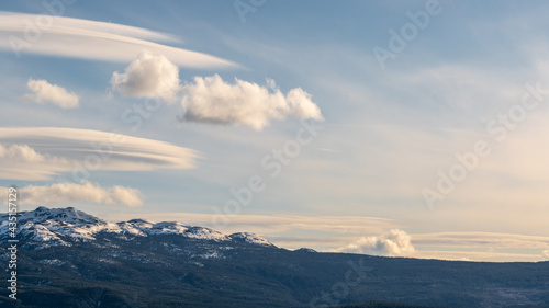 Blue sky day with wispy clouds, pink toned sunset and snow capped mountains below with stunning landscape background. 