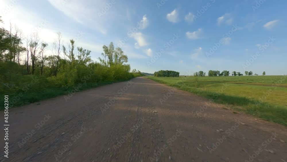Rural scene. A motorcyclist drives along a paved road near a field. Bright blue sky, low trees in the sun. Camera forward. High quality. 4k footage. Rural scene. A motorcyclist drives along a paved road near a field. Bright blue sky, low trees in the sun. Camera forward. High quality. 4k footage.