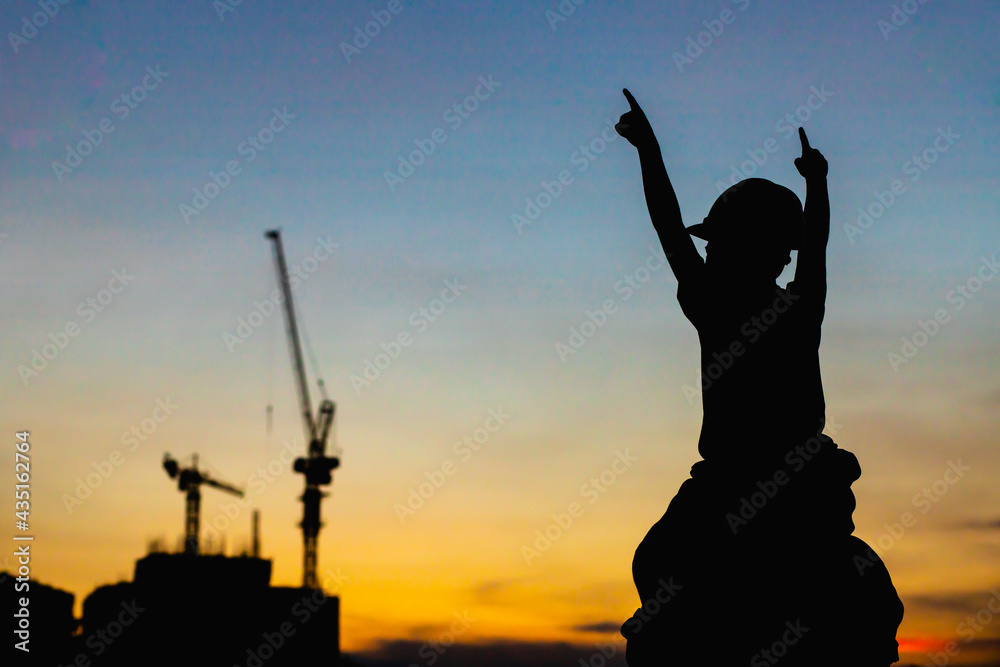 The silhouette of the happy father and son wearing a construction helmet holding hands expressing the joy of the sunset