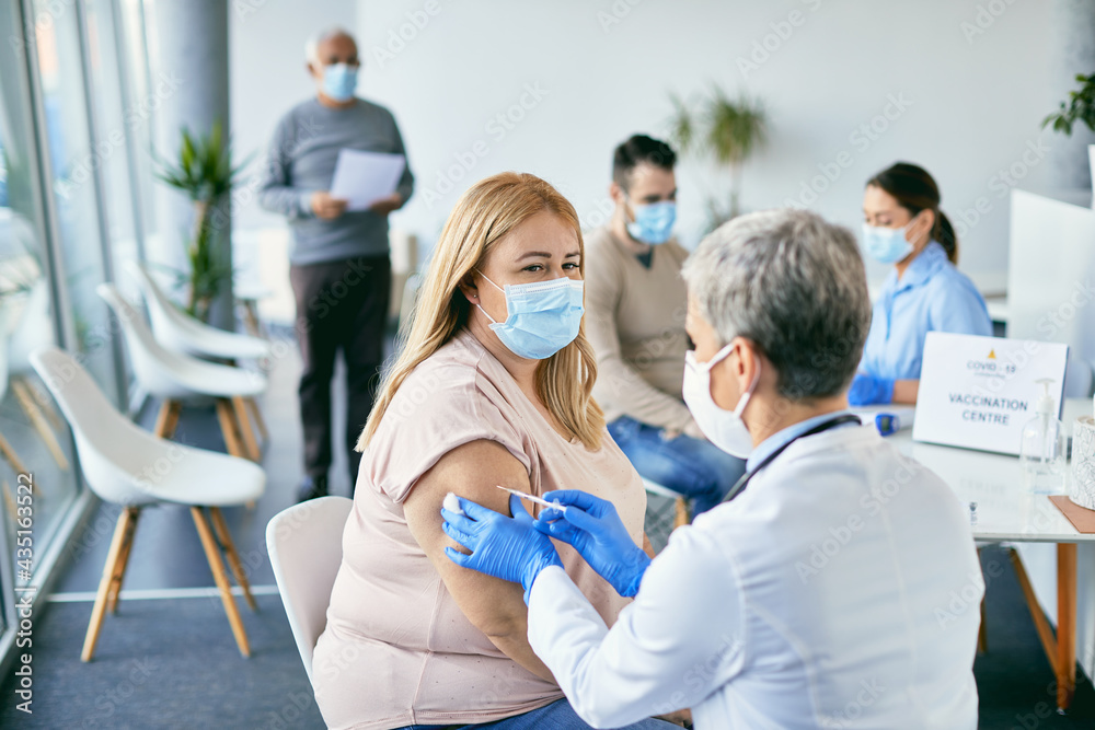 Fototapeta premium Woman with face mask getting vaccinated against coronavirus at vaccination center.