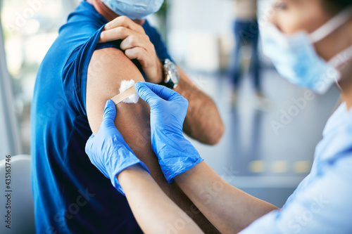 Tableau sur toile Close-up of nurse putting band aid on man's arm after coronavirus vaccination