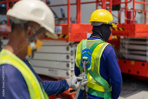 Workers preparing for working on a Scissor Lift Platform. Worker helping to check to condition of safety harness for team colleague.