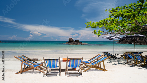 Several deck chairs were set up on the beautiful blue sea beach. Under the canopy of large trees © Jakachai