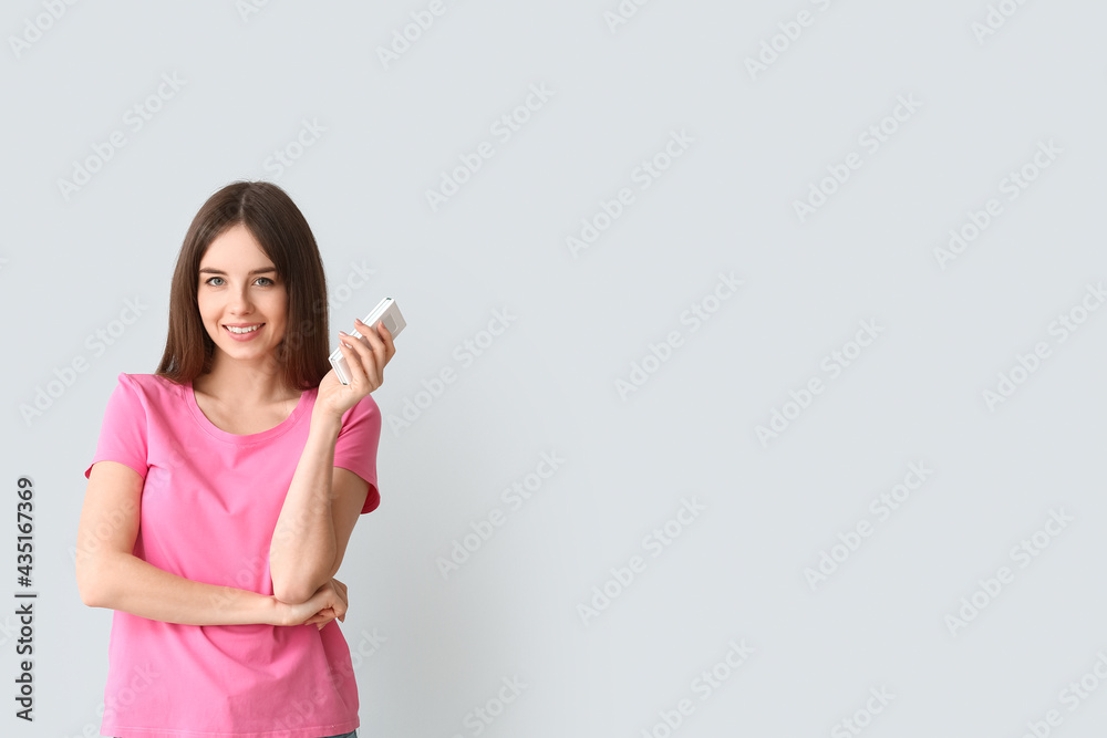 Young woman with air conditioner remote control on light background Young woman with air conditioner remote control on light background
