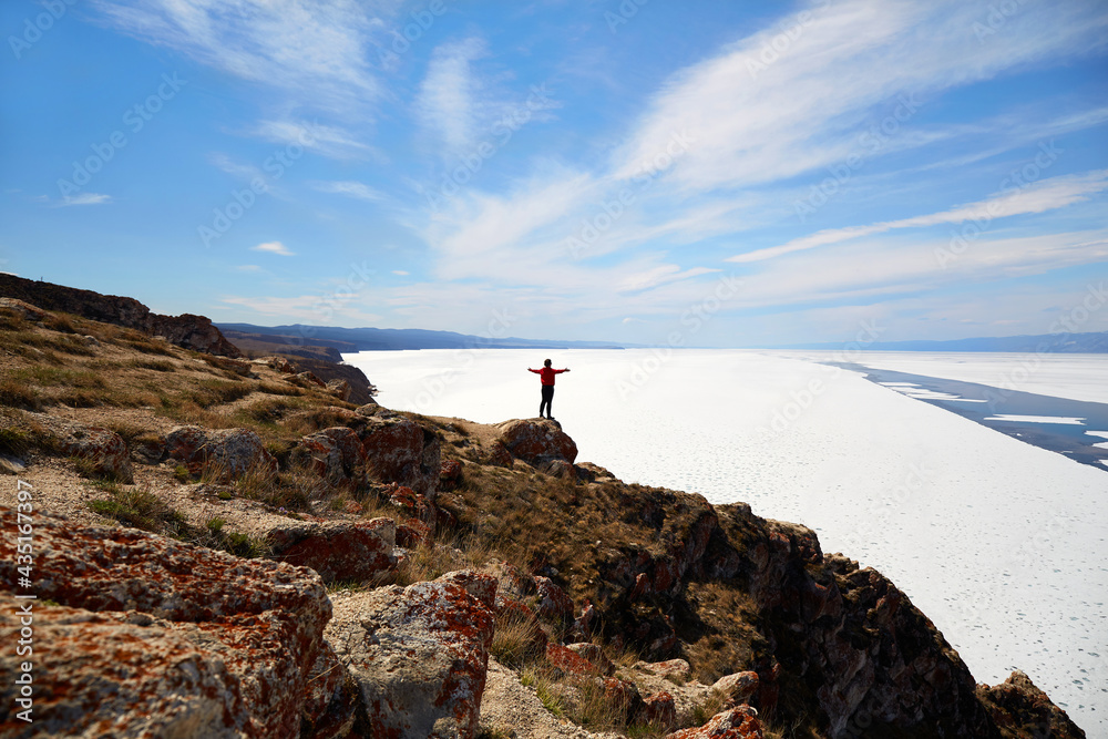 Lake Baikal in the spring. The girl stands on a rock and looks at the endless expanses of the lake. Time to release the lake from the ice.