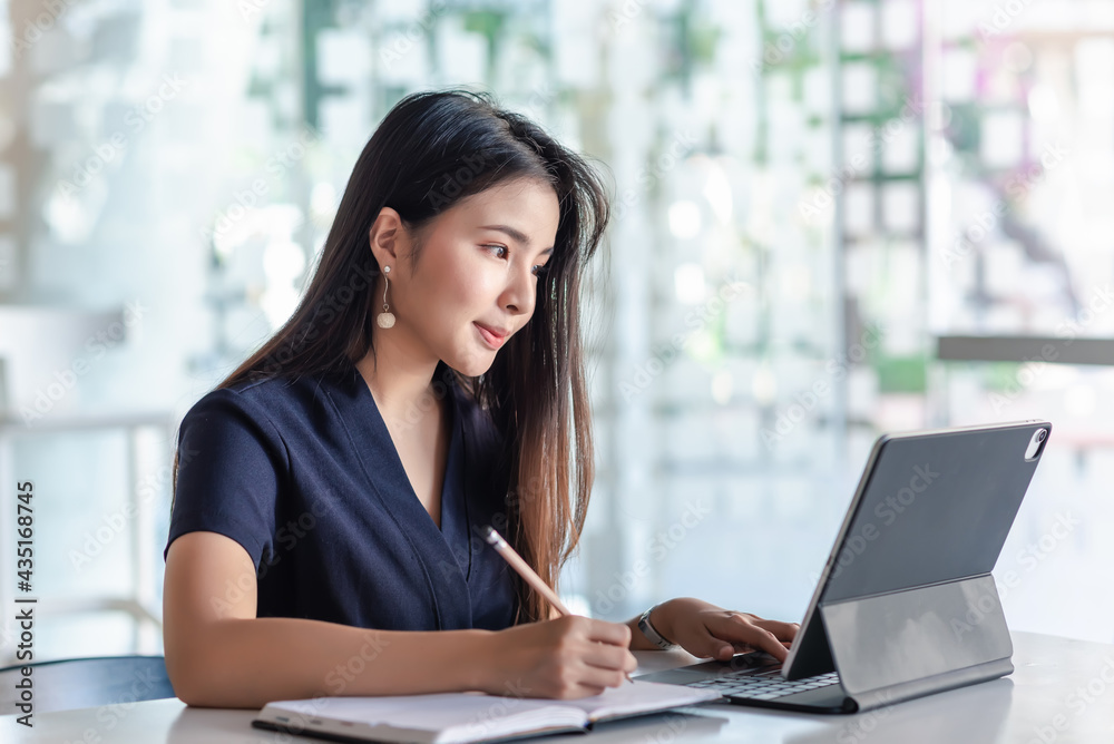 Beautiful Asian businesswoman taking notes and using tablet at the office. Beautiful Asian businesswoman taking notes and using tablet at the office.